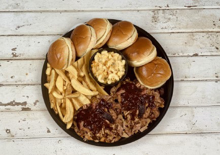 The Flying Pig Feast with chicken wings, ribs, cornbread muffins, celery sticks, pickles, and a bowl of mac and cheese piled high on a black platter